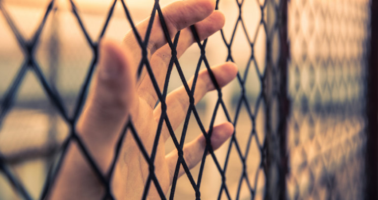 Person in prison looking out from fencing.